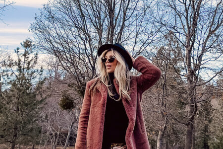 casual 70s boho look-floral bell bottom flares-faux fur coat-blonde woman standing on a tree-lined street with fall colors and leaves and blue cloudy skies