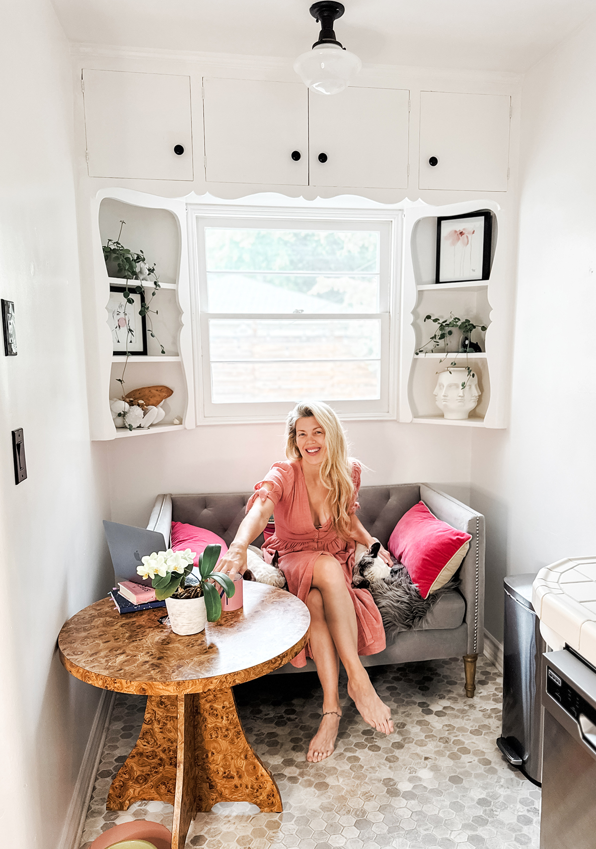 sitting in my kitchen nook in a pink dress with my dogs on a grey settee sofa