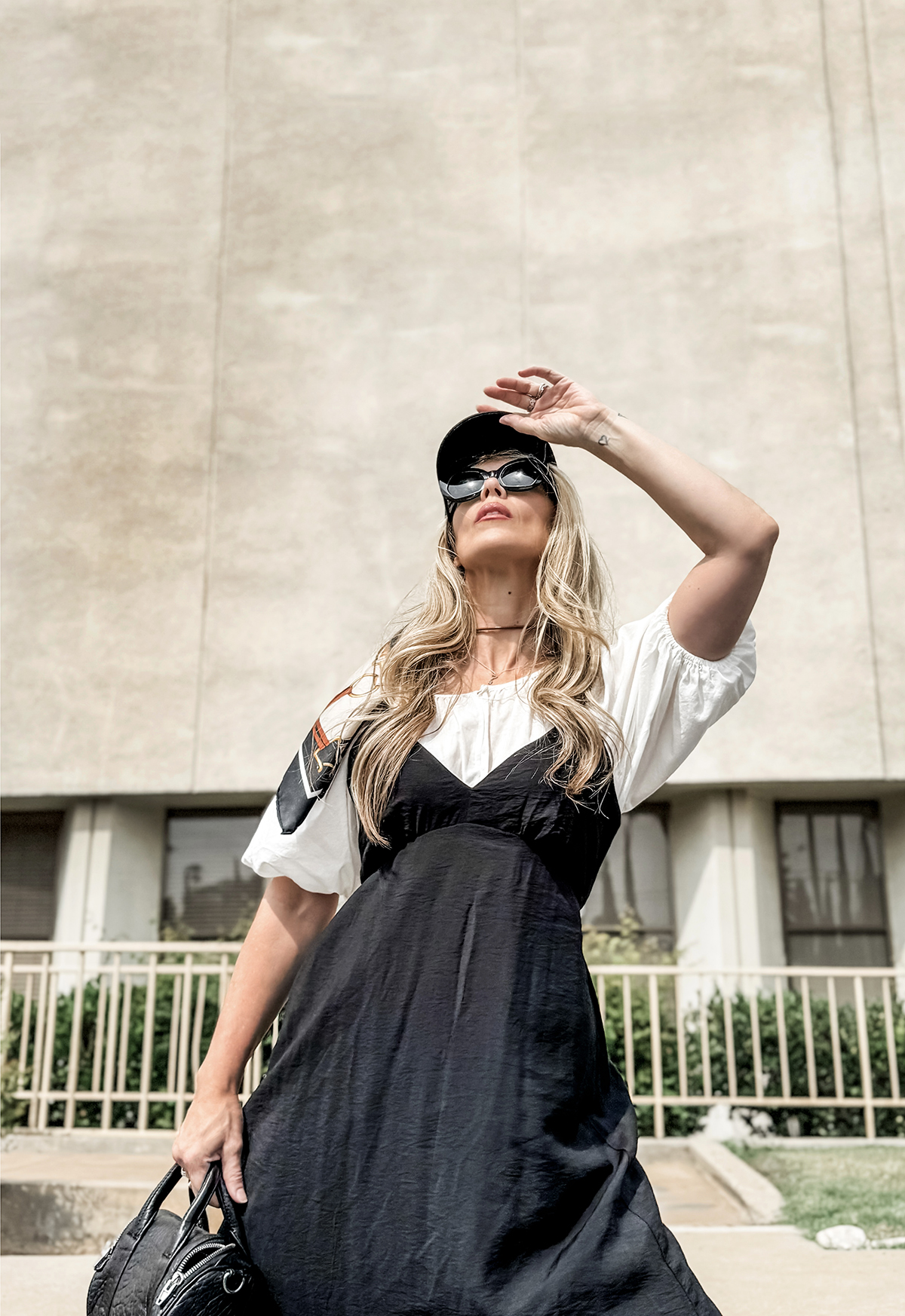 love Maegan fashion style blog wearing black long maxi dress from target layered over a white blouse with puff sleeves and a baseball hat with a vintage scarf tied on the back standing in front of a mid century modern building in California