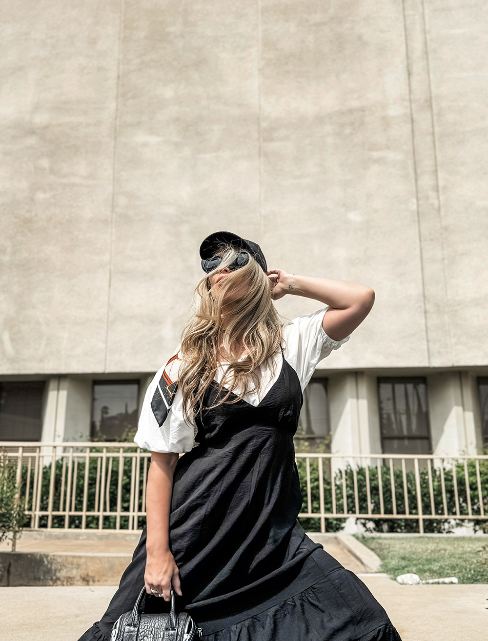 black summer sun dress layered over a white pouf sleeve blouse with a baseball cap and sunglasses